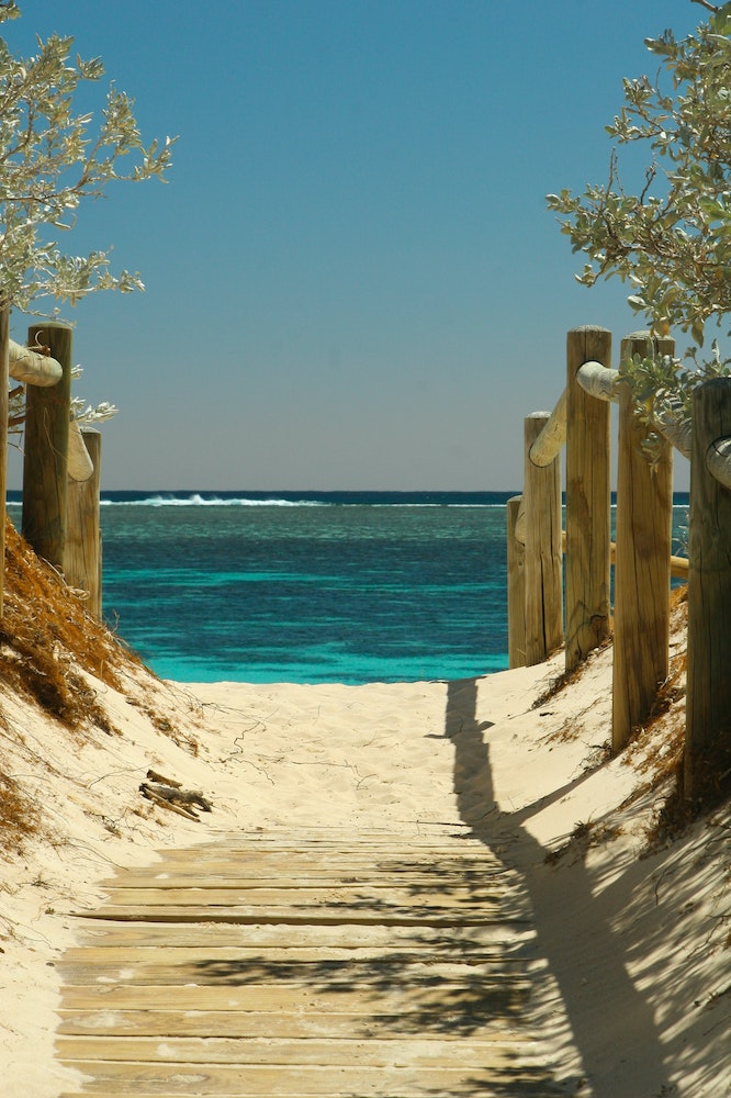 Wooden fencing and sandly pathway leading to blue ocean